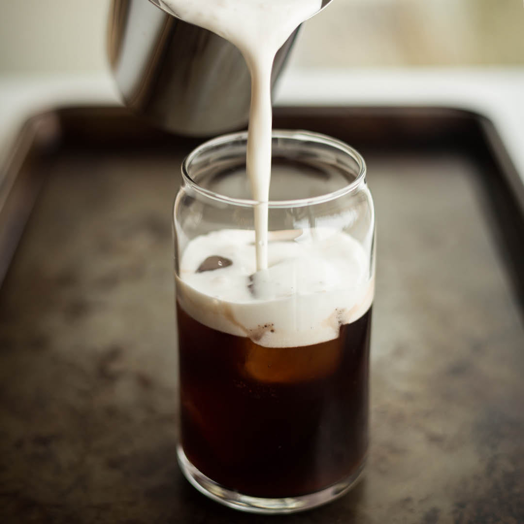 Cream poured into glass cup containing Iced Mocha Mushroom Herbal Tea